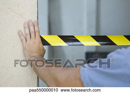 Stock Image - Worker placing safety tape across doorway. Fotosearch