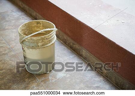 Picture - Bucket set on tiled floor near ledge. Fotosearch