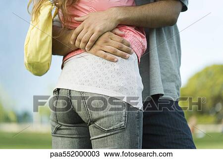 Stock Image - "Young couple embracing, mid section, low angle view". Fotosearch