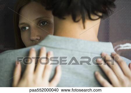 Stock Image - "Young couple embracing, woman looking away". Fotosearch