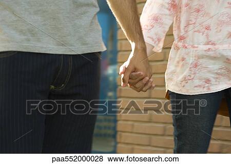 Stock Photo - "Young couple holding hands, walking, cropped view". Fotosearch