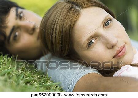 Stock Photo - "Young couple lying on grass, looking at camera, close-up". Fotosearch