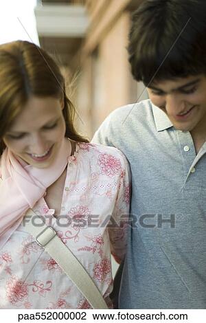 Stock Image - "Young couple side by side, looking down, smiling". Fotosearch