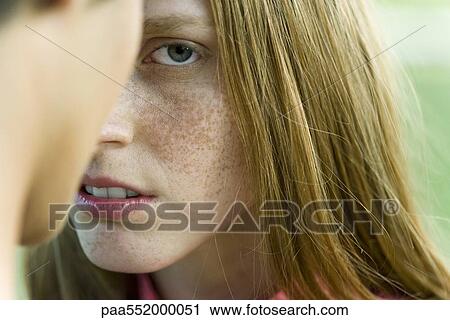 Stock Image - "Young woman facing man, staring warily at camera, cropped". Fotosearch