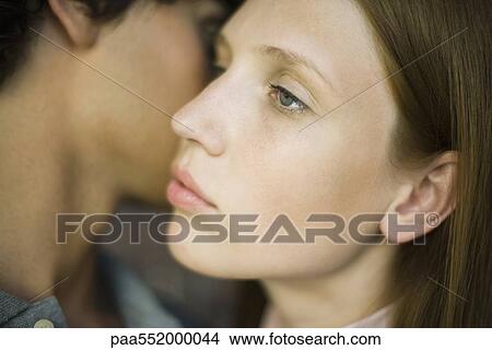 Picture - Young woman looking away distantly as man kisses her cheek. Fotosearch