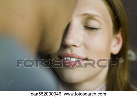Stock Photograph - "Young woman smiling as man kisses her forehead, eyes closed". Fotosearch