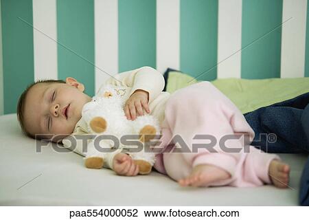 Stock Image - Baby sleeping in crib, holding stuffed toy. Fotosearch