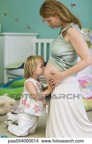 Picture - Little girl kissing mother's pregnant belly. Fotosearch