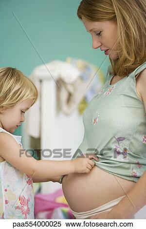 Stock Photography - Little girl looking at mother's pregnant belly. Fotosearch