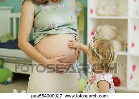 Stock Photo - Little girl touching mother's pregnant belly. Fotosearch