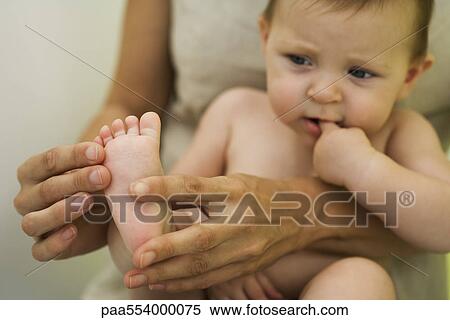 Stock Photography - Mother holding baby on lap, playing with baby's foot, cropped. Fotosearch
