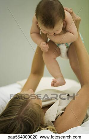 Stock Image - Mother lying on back holding up baby. Fotosearch