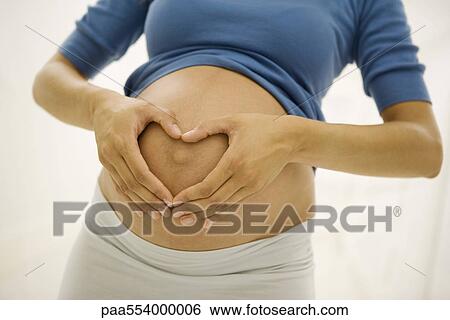 Stock Photograph - Pregnant woman holding hands in heart shape around navel. Fotosearch