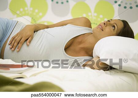 Pregnant woman lying on bed, smiling, looking up View Large Photo Image Stock Photo - Pregnant woman lying on bed, smiling, looking up. Fotosearch