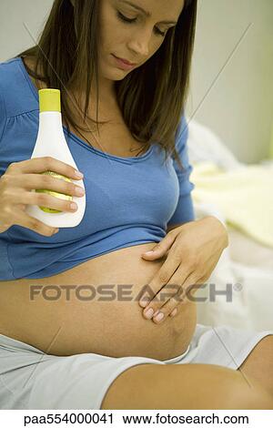 Stock Image - Pregnant woman moisturizing stomach. Fotosearch