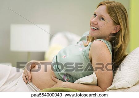 Stock Photo - Pregnant woman relaxing on bed, smiling. Fotosearch