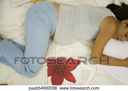 Stock Photograph - Pregnant woman sleeping on side, books nearby. Fotosearch