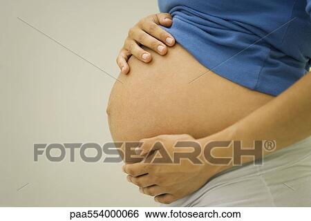 Stock Photograph - Woman holding pregnant belly, side view. Fotosearch