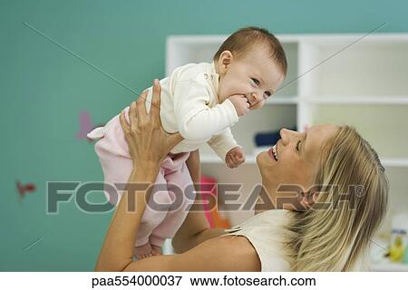 Stock Photo - Young mother holding up baby, smiling. Fotosearch