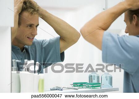 Stock Photo - Man looking at self in mirror, fixing hair. Fotosearch