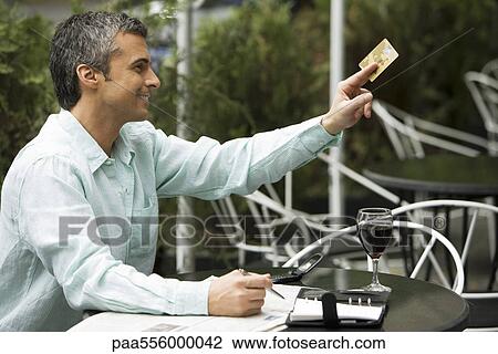 Stock Image - Man sitting in outdoor cafe, holding out credit card to pay. Fotosearch