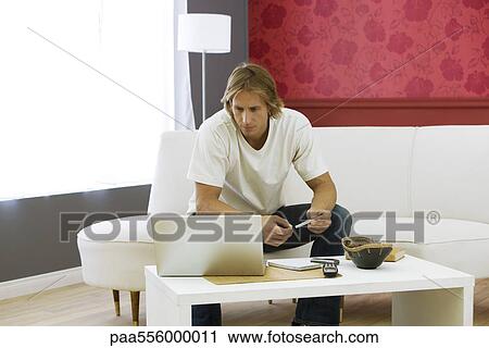 Man sitting on sofa in living room, using laptop set on coffee table View Large Photo Image Stock Image - Man sitting on sofa in living room, using laptop set on coffee table. Fotosearch
