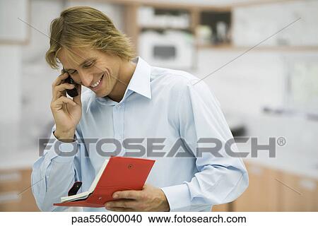 Man using cell phone, looking at agenda View Large Photo Image Stock Image - Man using cell phone, looking at agenda. Fotosearch