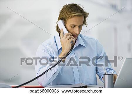 Man using phone and laptop computer at desk View Large Photo Image Stock Photography - Man using phone and laptop computer at desk. Fotosearch
