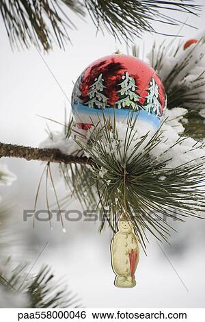 Stock Photograph - Christmas ornaments hanging on snow-covered branch. Fotosearch