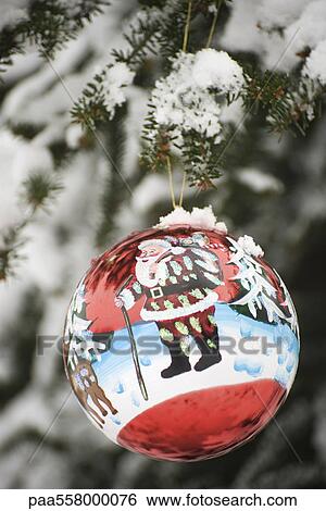 Stock Photograph - Colorful Christmas ornament hanging from snow frosted branch. Fotosearch