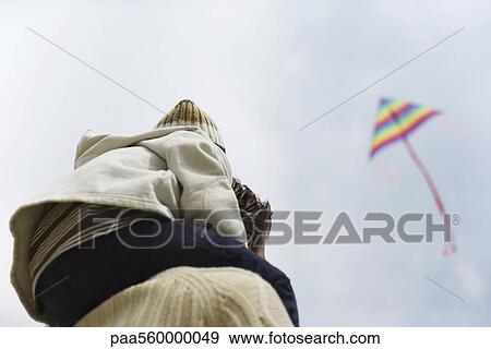 Child sitting on father's shoulders, looking at kite in sky View Large Photo Image Stock Photo - Child sitting on father's shoulders, looking at kite in sky. Fotosearch