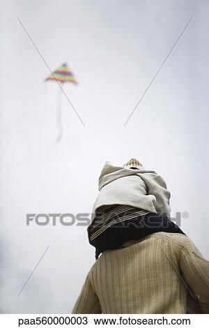 Stock Image - Father holding son on shoulders, kite flying in sky in background. Fotosearch