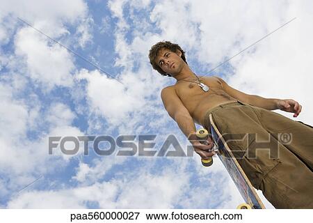 Young man holding skateboard, looking away with furrowed brow View Large Photo Image Stock Photo - Young man holding skateboard, looking away with furrowed brow. Fotosearch