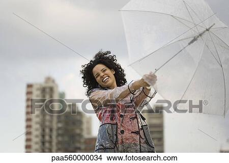 Young woman holding onto umbrella on windy day, laughing View Large Photo Image Picture - Young woman holding onto umbrella on windy day, laughing. Fotosearch