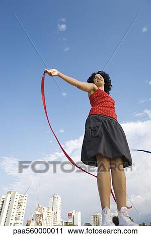 Young woman holding ribbon in wind, smiling, low angle view View Large Photo Image Stock Image - Young woman holding ribbon in wind, smiling, low angle view. Fotosearch