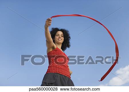 Young woman holding ribbon in wind, smiling, low angle view View Large Photo Image Stock Photo - Young woman holding ribbon in wind, smiling, low angle view. Fotosearch
