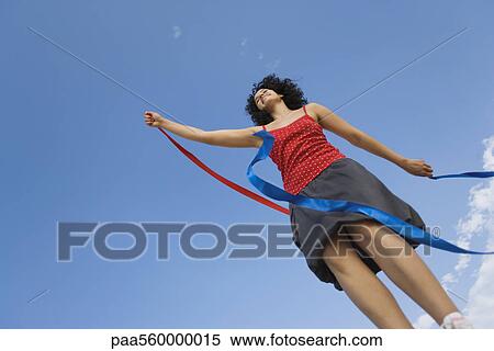 Young woman holding ribbon in wind, smiling, low angle view View Large Photo Image Stock Photography - Young woman holding ribbon in wind, smiling, low angle view. Fotosearch