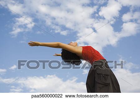 Young woman leaning backwards with arms extended, sky in background View Large Photo Image Stock Image - Young woman leaning backwards with arms extended, sky in background. Fotosearch