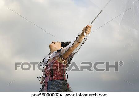 Young woman standing outdoors on rainy day, letting rain fall on her face View Large Photo Image Picture - Young woman standing outdoors on rainy day, letting rain fall on her face. Fotosearch