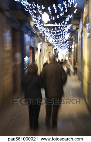 Stock Image - Couple walking down alley illuminated by Christmas lights at night. Fotosearch