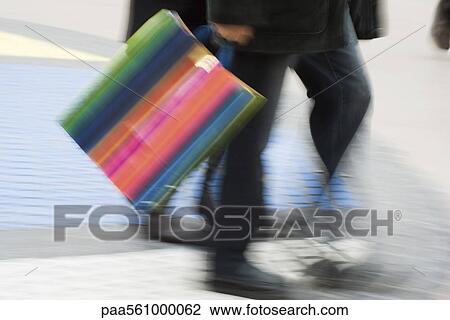 Stock Image - Pedestrian carrying shopping bag, blurred. Fotosearch