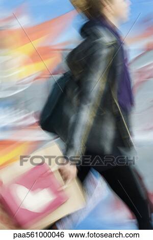 Stock Photograph - Shopper carrying shopping bags, blurred. Fotosearch