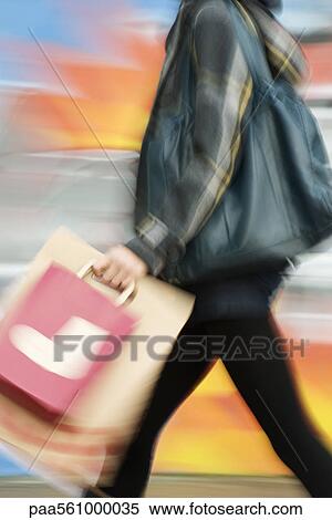Stock Photography - Shopper walking with shopping bags, blurred. Fotosearch