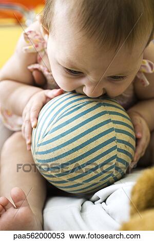 Stock Image - Infant chewing on striped ball. Fotosearch