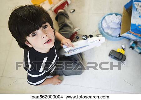 Picture - Little boy sitting on floor playing with toys, looking up at camera. Fotosearch