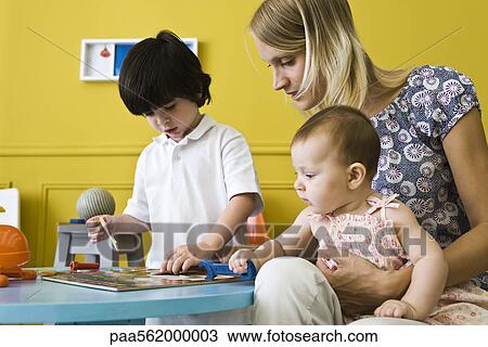 Stock Image - Little boy working jigsaw puzzle with mother and infant sister. Fotosearch