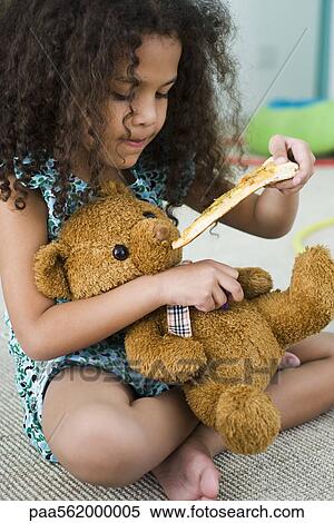 Stock Photography - Little girl feeding teddy bear pizza. Fotosearch