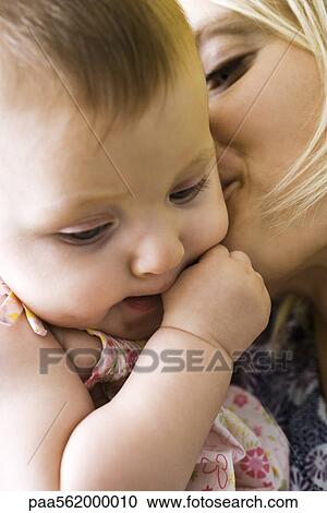 Stock Image - Mother kissing infant's cheek, close-up. Fotosearch