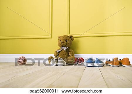 Teddy bear sitting on floor with several pairs of shoes, ball nearby View Large Photo Image Stock Image - Teddy bear sitting on floor with several pairs of shoes, ball nearby. Fotosearch