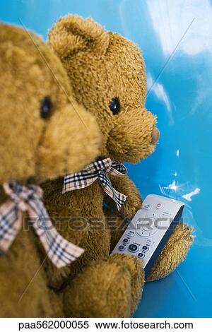 Stock Photography - Teddy bears sitting side by side, one holding remote control. Fotosearch